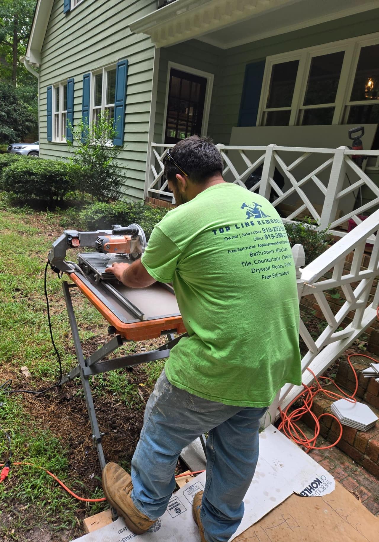 A Top Line Remodel crew member in a branded shirt cutting tile on a wet saw outside a customer's home