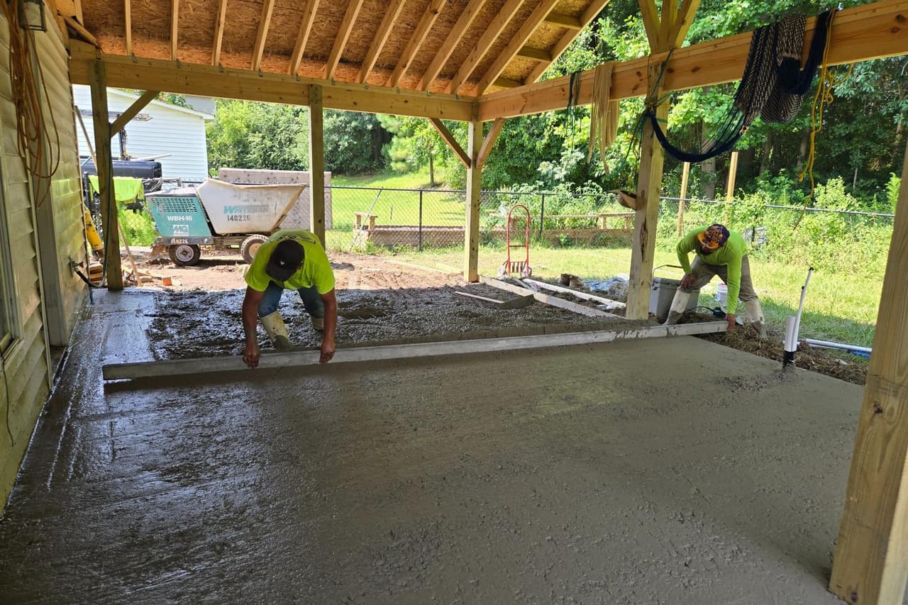 Two Top Line Remodel crew members screeding a fresh concrete slab under a newly framed covered porch