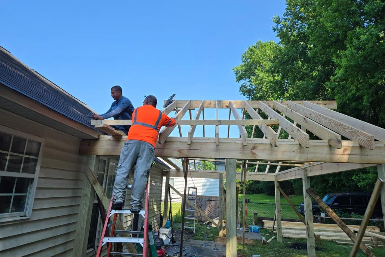 Two Top Line Remodel crew members framing the roof of a new covered addition against a clear blue sky
