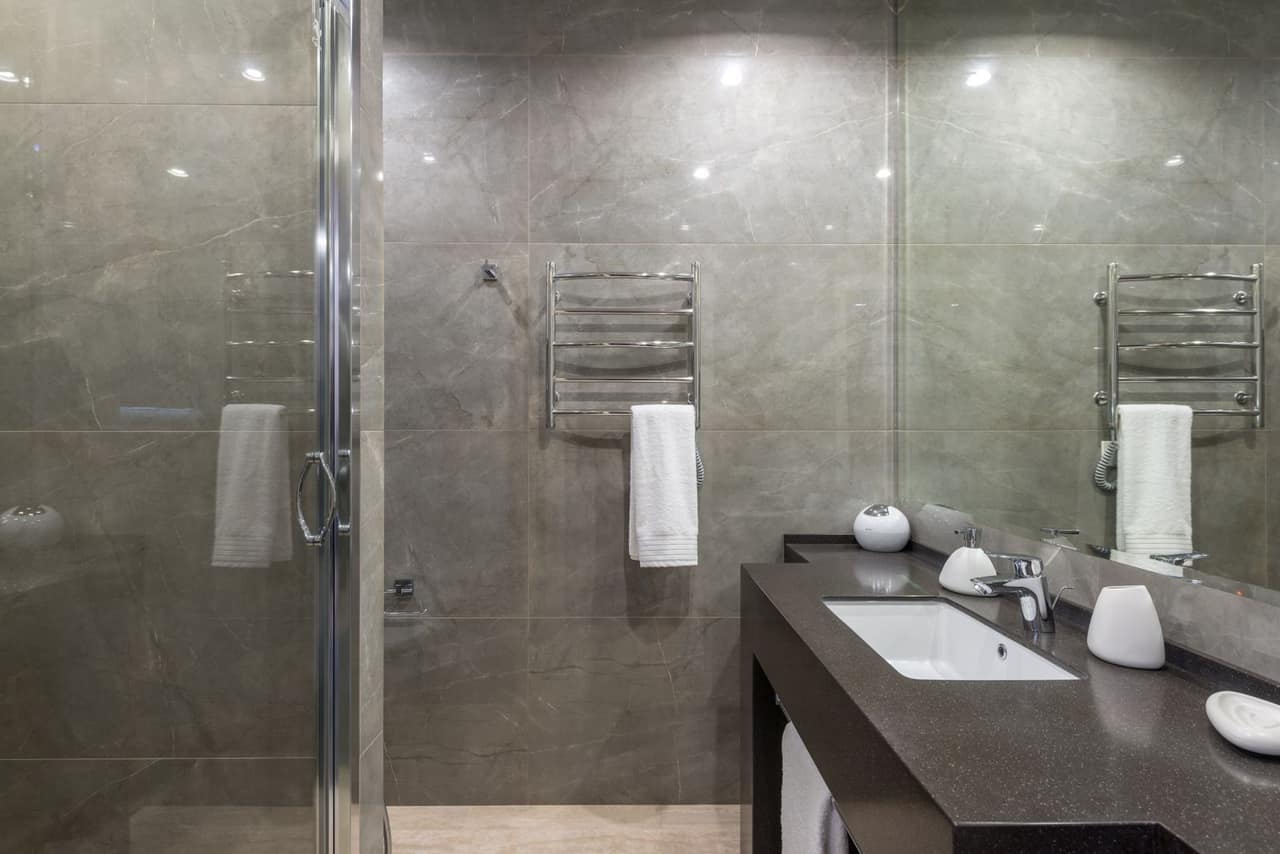 A finished bathroom with large-format stone-look wall tile, a glass shower enclosure and a stone vanity top