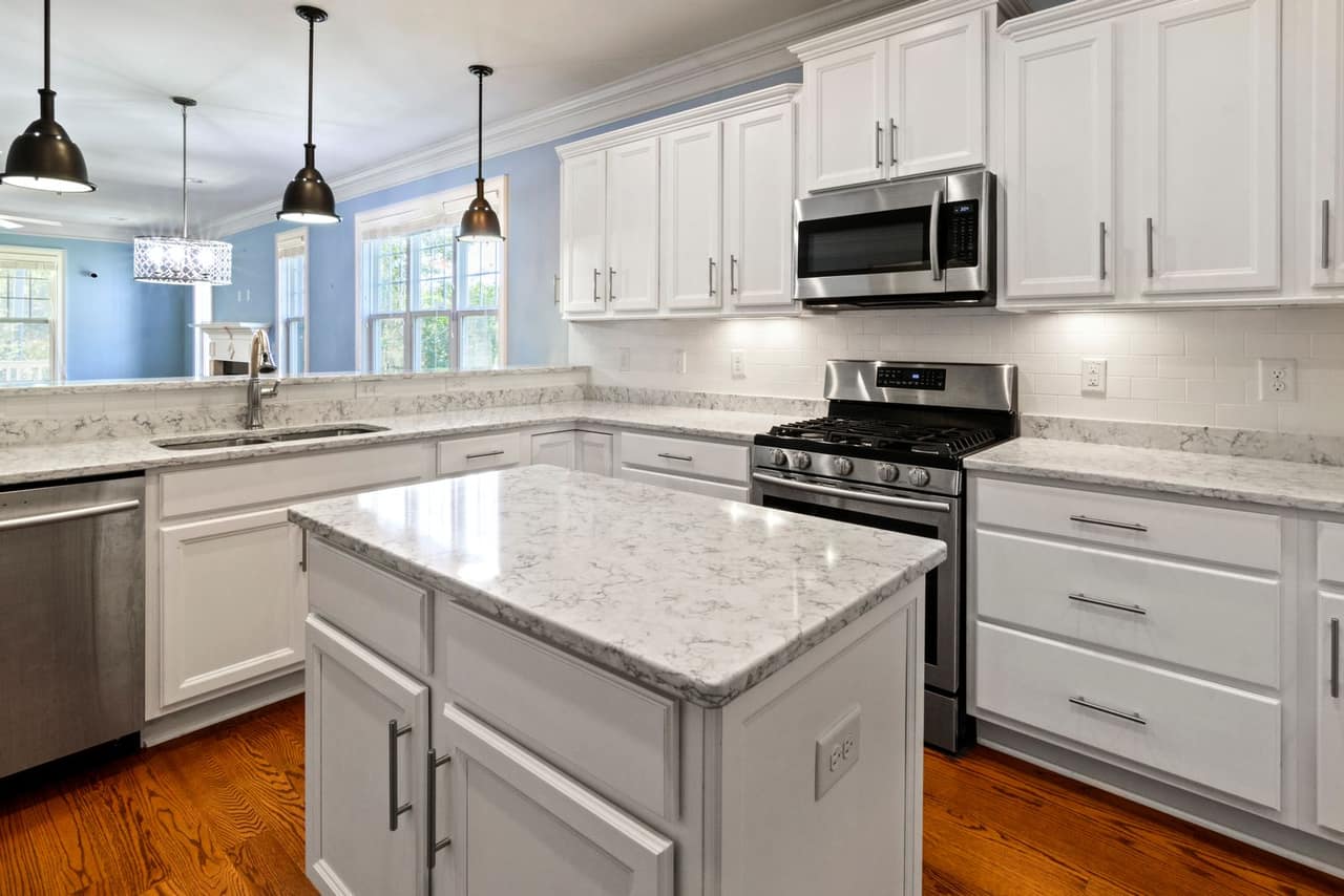 A finished kitchen island and perimeter run in white shaker cabinetry with veined stone countertops