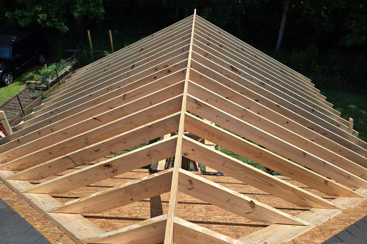 Newly framed roof rafters meeting a ridge board, seen from above on a bright day