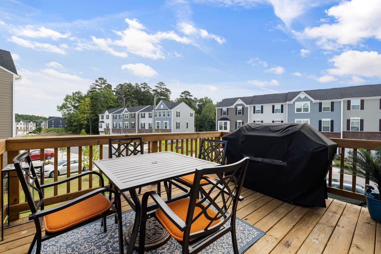 A finished raised wooden deck with railing, table and chairs, looking out over a suburban neighbourhood