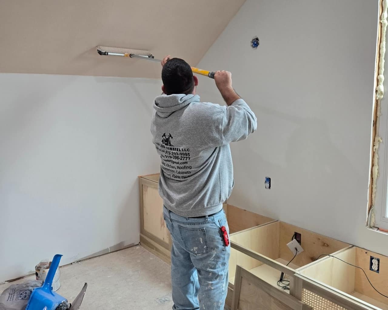 A Top Line Remodel crew member in a branded hoodie rolling a freshly finished sloped ceiling with a pole roller