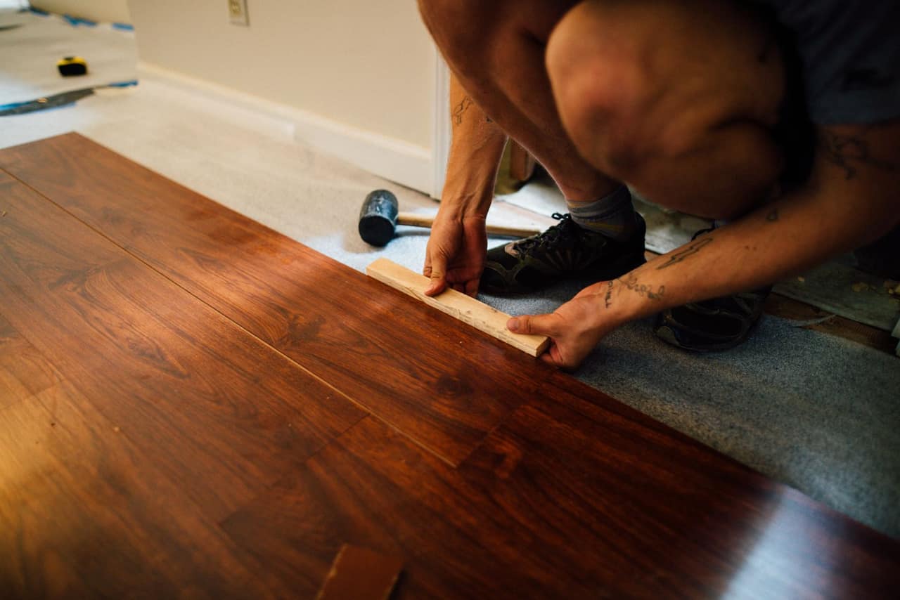 Dark wood-effect floor planks being laid over underlayment with a tapping block and mallet