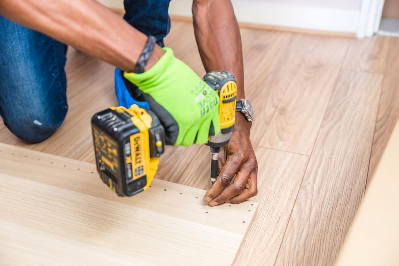 Gloved hands driving a screw into a floor threshold with a cordless drill