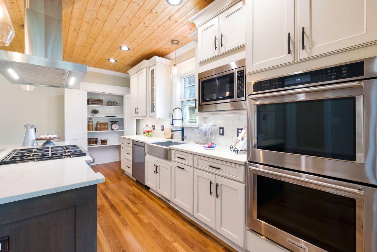 A finished kitchen with white shaker cabinets, stone countertops, a subway tile backsplash and stainless wall ovens