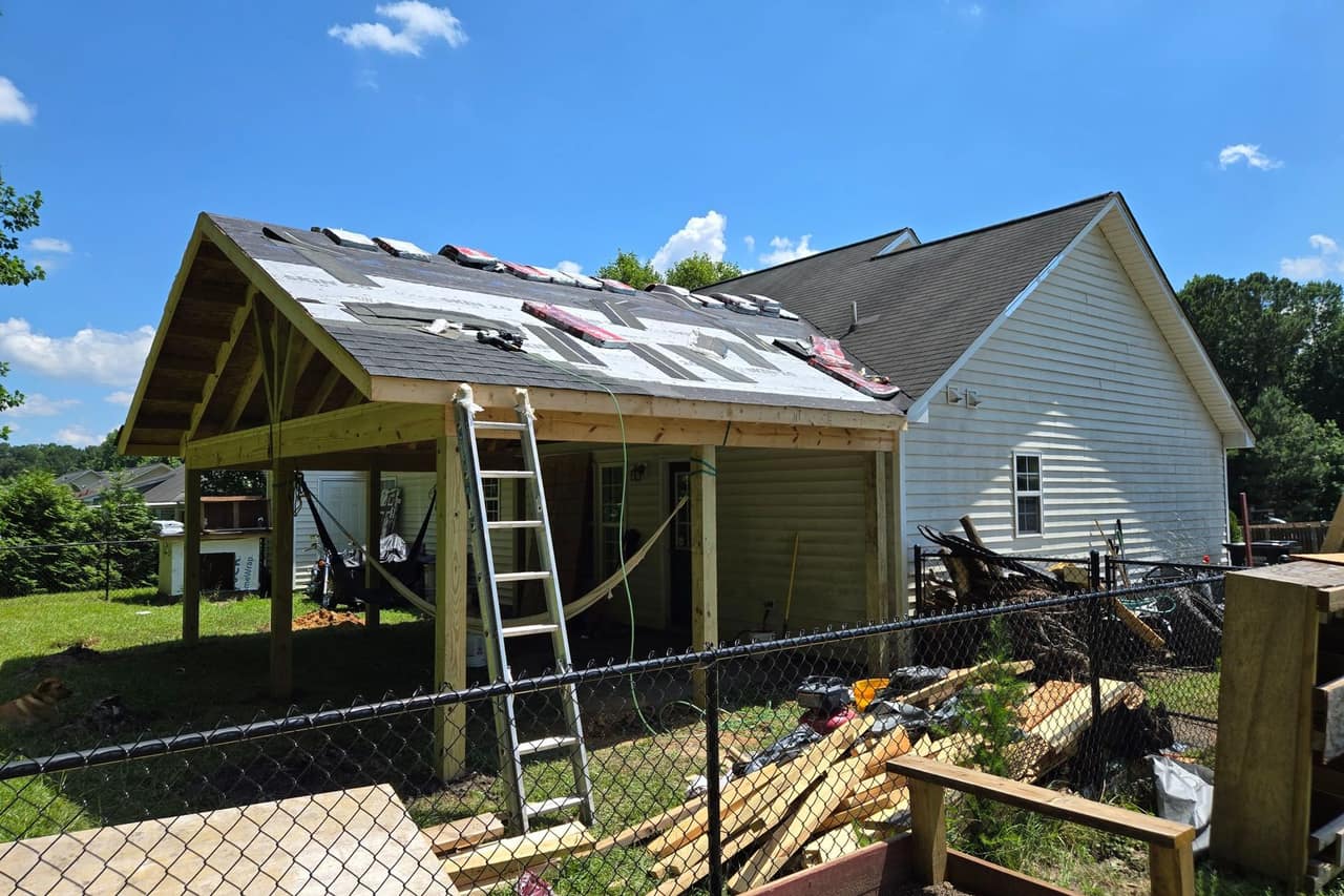 A covered porch being built and tied into the existing roofline of a house, with underlayment down and framing exposed