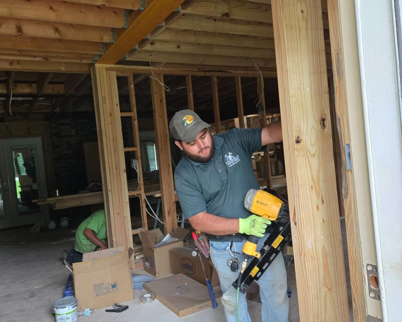 A house opened up to bare studs and joists under a new engineered beam, with a Top Line Remodel crew member framing a new opening